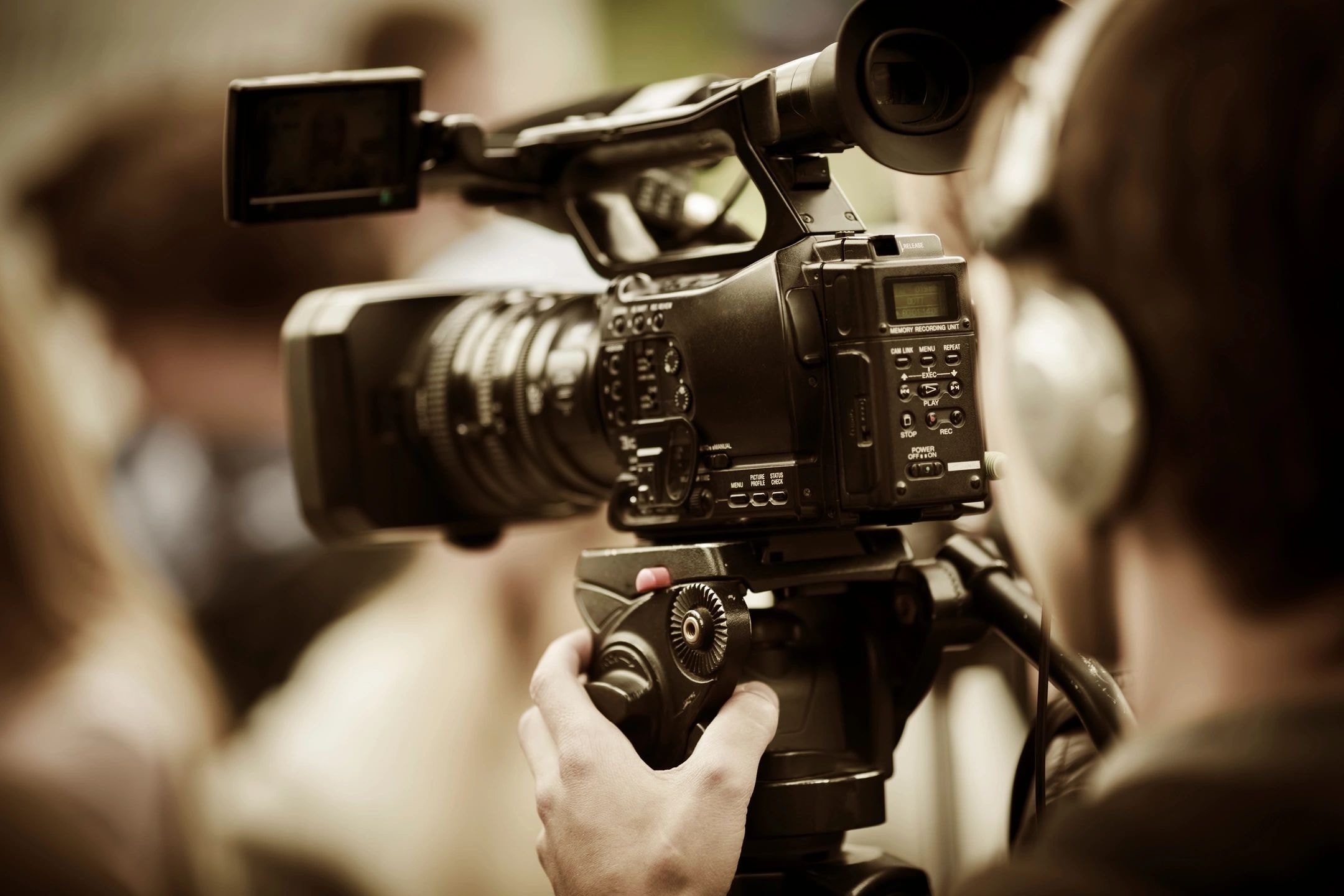 Cameraman operating a video camera mounted on a tripod at an event