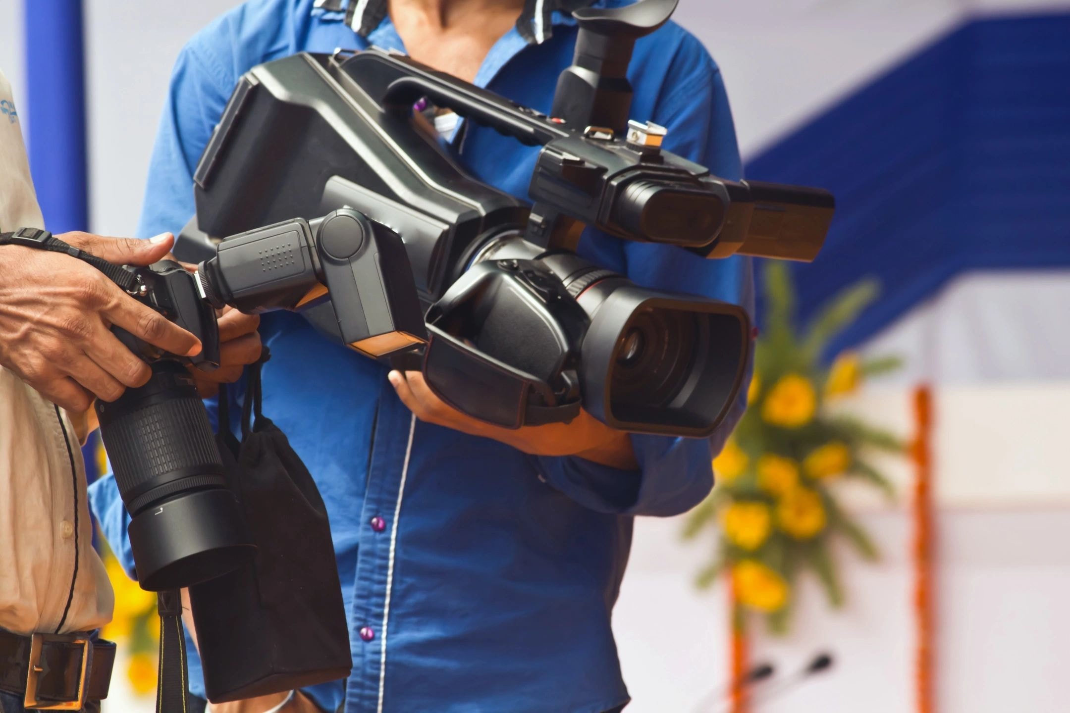 Two videographers holding professional camera equipment at a press event
